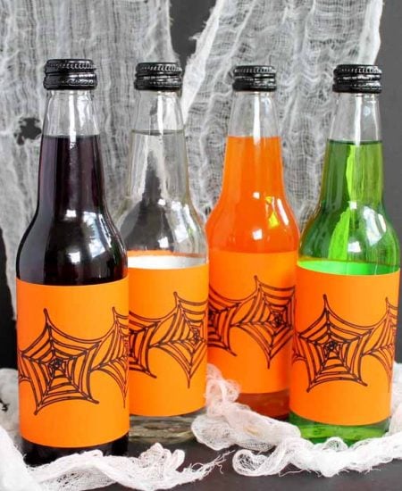 different colors of glass drinks with orange Halloween labels on spider web backdrop
