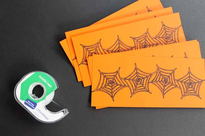 orange Halloween drink labels with spider webs and tape dispenser