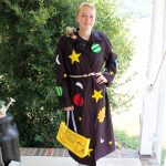 A woman holding a bus sign posing for the camera with a Miss Frizzle costume on