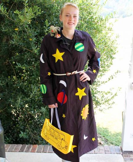 A woman holding a bus sign posing for the camera with a Miss Frizzle costume on