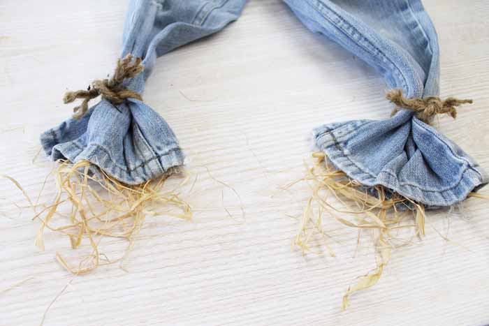 tying the legs of jeans and stuffing with straw to make a scarecrow