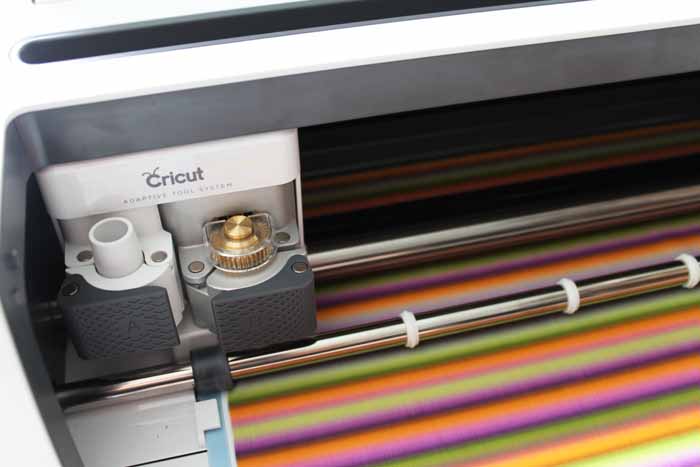 A close up of a Cricut maker with striped fabric