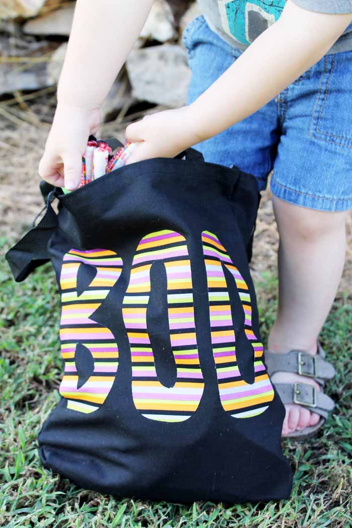 A little boy that is standing in the grass putting candy in his trick or treat bag