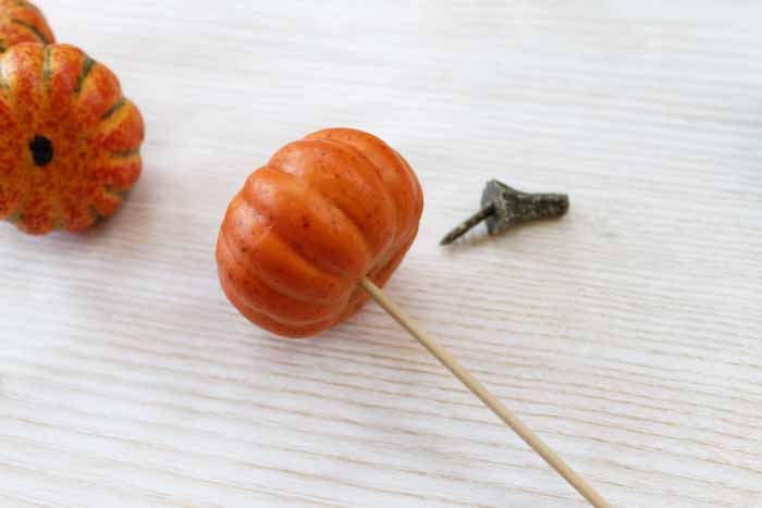 Removing the stem from a plastic pumpkin and putting it on a wooden stick
