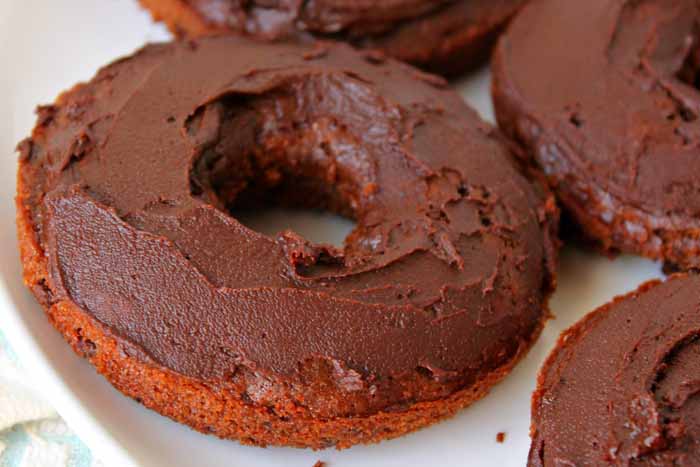 A close up of a piece of a baked chocolate cake donut with chocolate icing.
