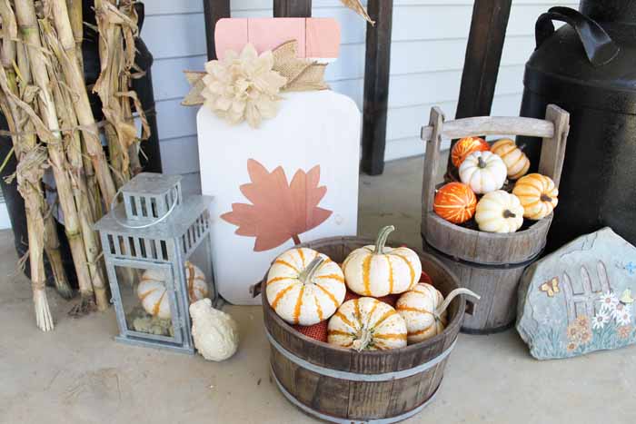 Wooden buckets of pumpkins and a wooden mason jar sign with maple leaf on a farmhouse style fall porch 