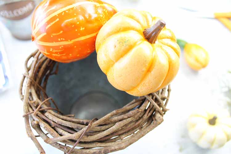 using hot glue to put pumpkins on a grapevine wreath