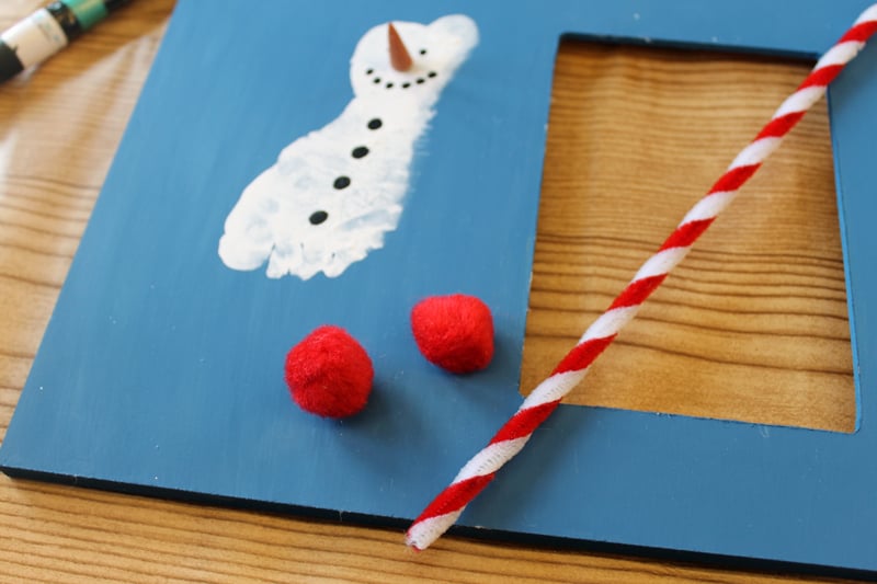 2 red pompoms and a candy cane striped pipe cleaner on a frame