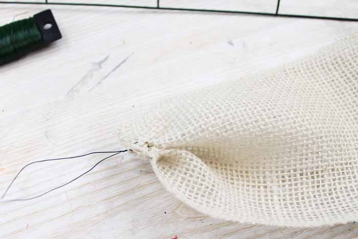 Learn how to make your own DIY candy cane wreath with these step by step instructions. Add this whimsical DIY Christmas wreath to your home! floral wire tied around end of white burlap ribbon