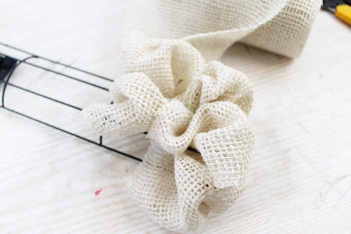 Learn how to make your own DIY candy cane wreath with these step by step instructions. Add this whimsical DIY Christmas wreath to your home! adding burlap ribbon in rows on a candy cane wreath form
