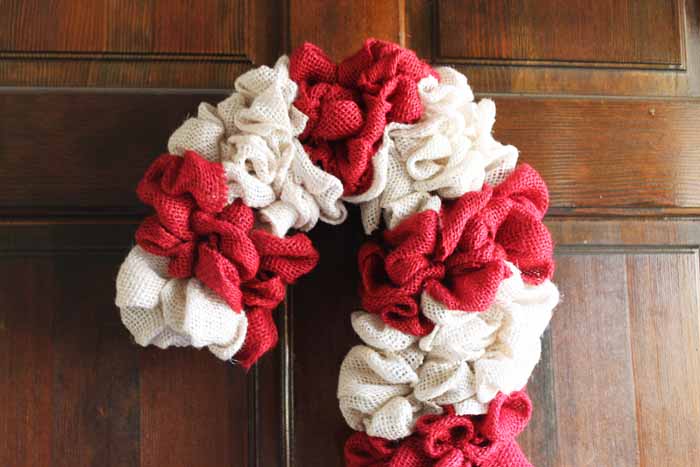 Learn how to make your own DIY candy cane wreath with these step by step instructions. Add this whimsical DIY Christmas wreath to your home! top of a candy cane wreath hanging on a door