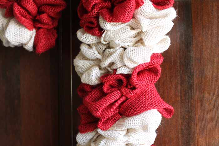 Learn how to make your own DIY candy cane wreath with these step by step instructions. Add this whimsical DIY Christmas wreath to your home! close up of a burlap wreath in red and white