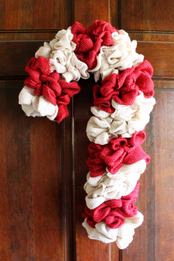 Learn how to make your own DIY candy cane wreath with these step by step instructions. Add this whimsical DIY Christmas wreath to your home! wood door with candy cane christmas wreath
