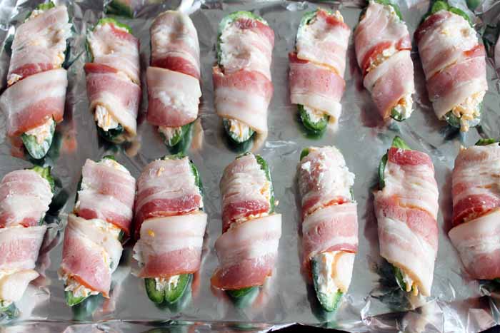 filled jalapenos wrapped in bacon on a cookie sheet