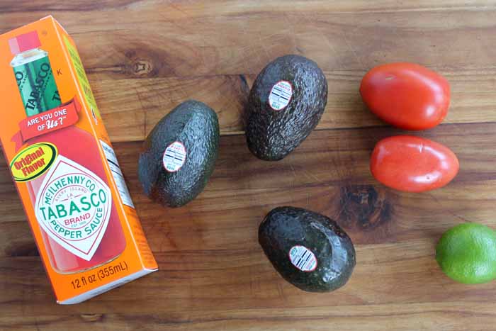 avocadoes, tomatoes, and tobasco sauce on a cutting board