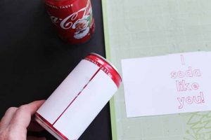 top shot showing how to tape paper to soda can for cheesy valentines