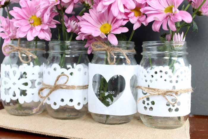 Close up of jars with different designs of cut felt wrapped around them and flowers inside.