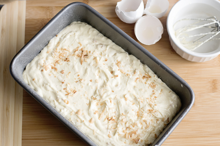 adding coconut to the top of cake batter in a pan