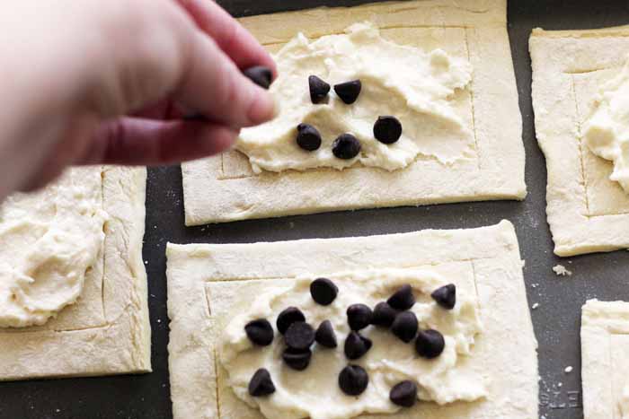 Adding chocolate chips to a cream cheese danish before baking.