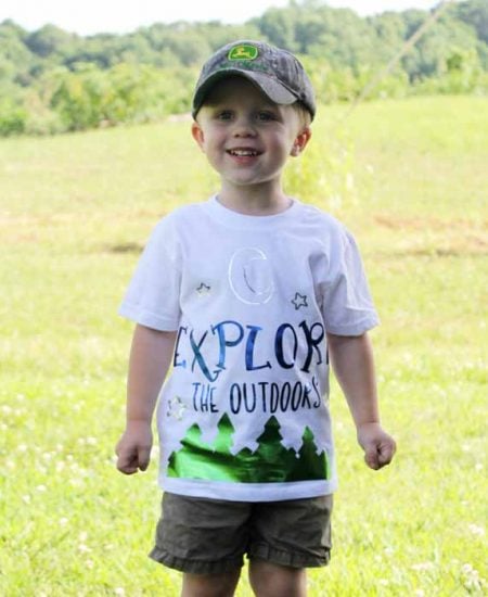 A young boy standing in a field wearing a camping shirt