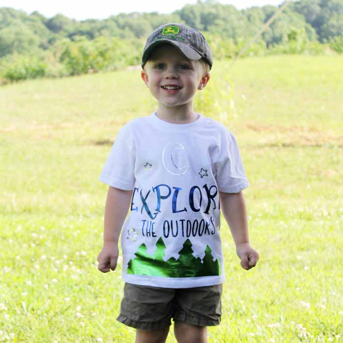 A young boy standing in a field wearing a camping shirt