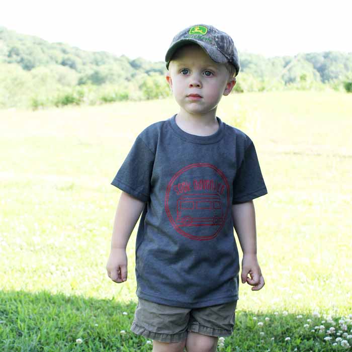 A little boy that is standing in the grass wearing a shirt about camping