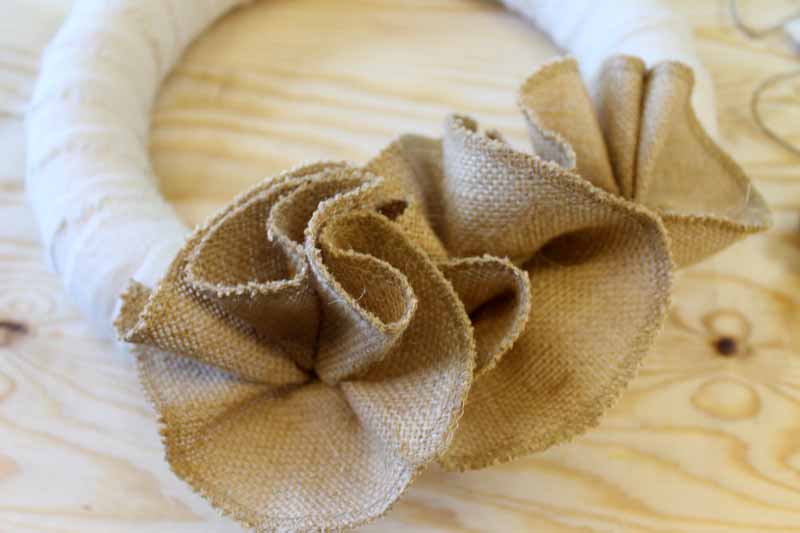 Using hot glue to secure burlap flowers to a wreath form.