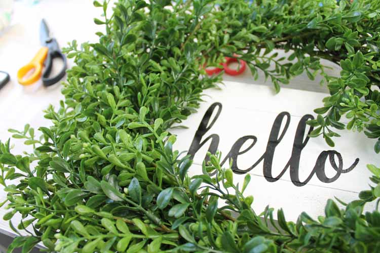 adding a green wreath to a white wood sign