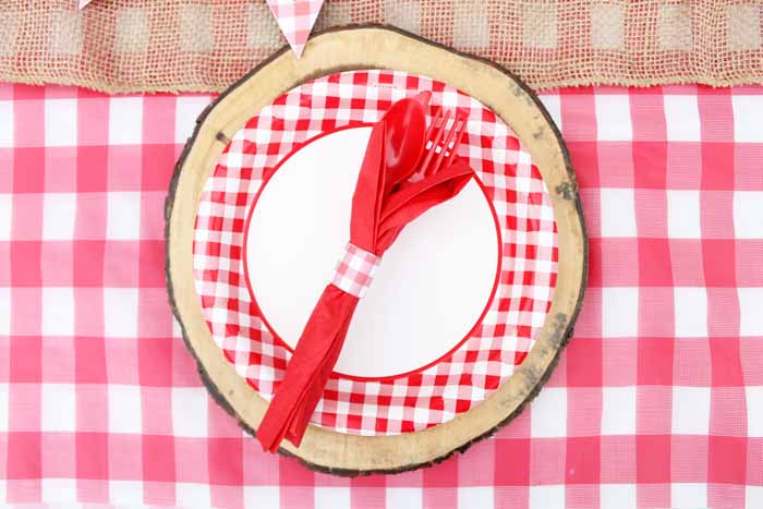 Festive checkered picnic plates set on wood place settings add a little rustic touch to your hot dog bar picnic