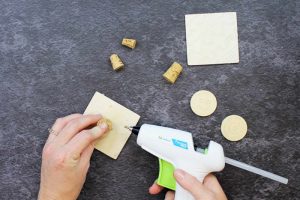 adding cork stopper to the back of a wood square with hot glue