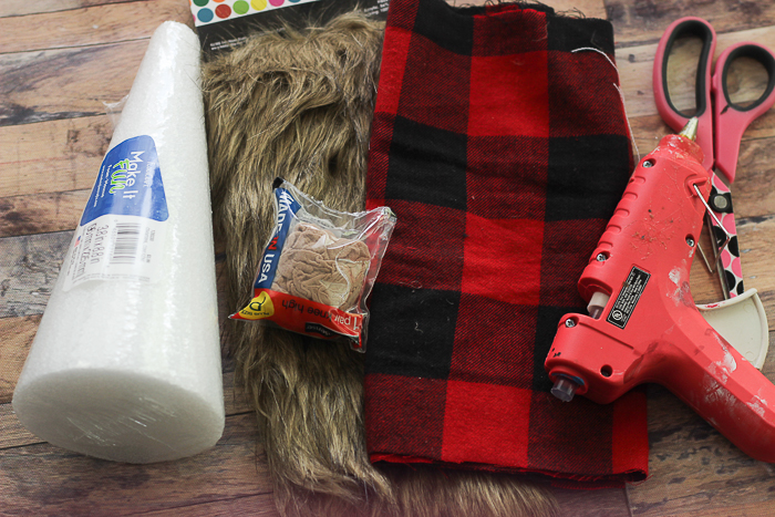 The supplies needed to make a Scandinavian gnome: a foam cone, faux fur, plaid fabric, and a hot glue gun