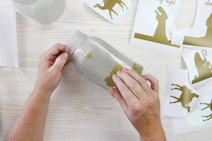 using transfer tape to add DIY nativity scene vinyl pieces to Christmas jars