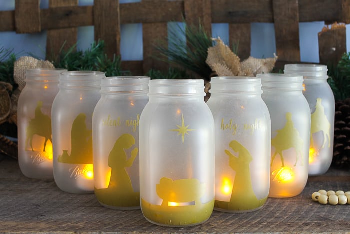 A group of glass mason jars on a table with lit candles inside