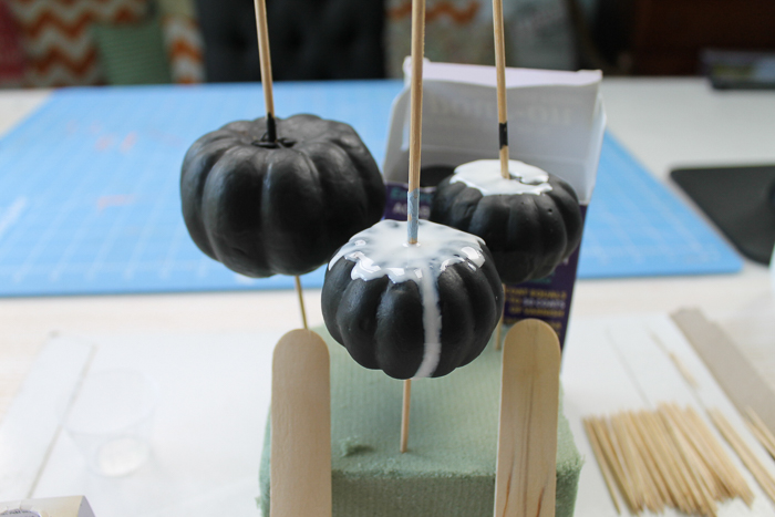 Pouring colored resin over black pumpkins to make marbled pumpkins.