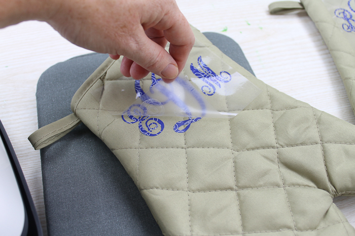 removing carrier sheet from blue floral Cricut patterned Iron-on applied to an oven mitt from the dollar store