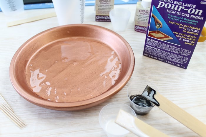 Pouring clear resin on a clay pot to make a cupcake stand.