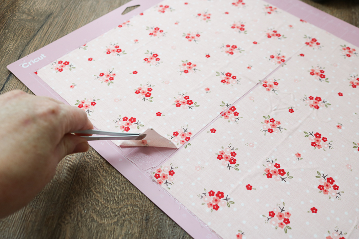 Removing pieces from fabric mat of Cricut Maker with tweezers.