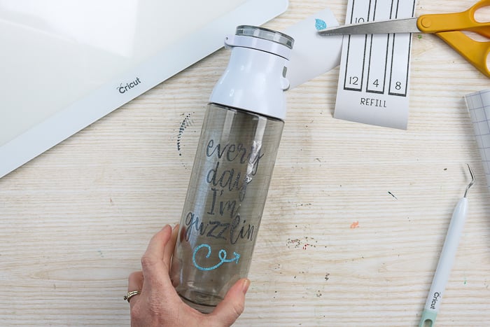 Adding glitter vinyl quote to the front of a water bottle.