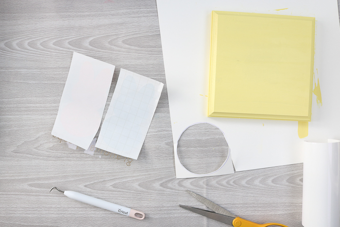 Adding cut vinyl with transfer tape to a painted yellow wood plaque.