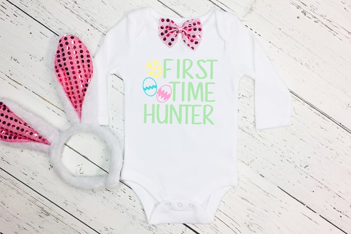 baby onesie with "first time hunter" on it and a pair of rabbit ears