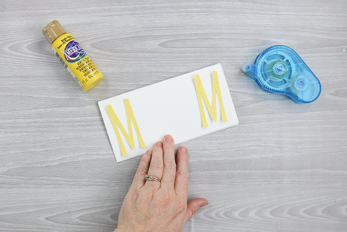 Using adhesive to adhere letters to a DIY card.