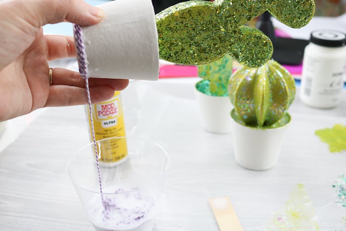 Wrapping twine with Mod Podge Ultra around a pot to decorate it.