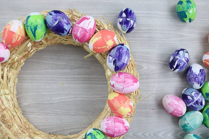 Using hot glue to secure marbled eggs to a wreath form.