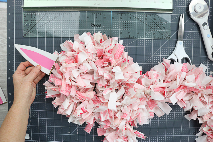 Adding ears to an Easter bunny rag wreath with hot glue.
