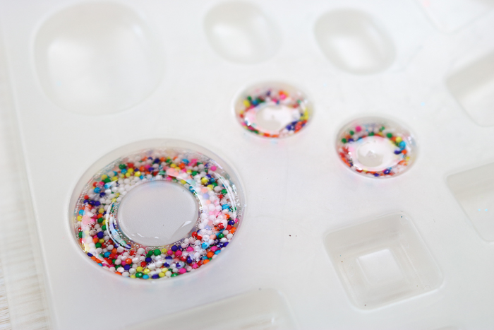 Pouring resin with sprinkles into a round mold to make donut charms.