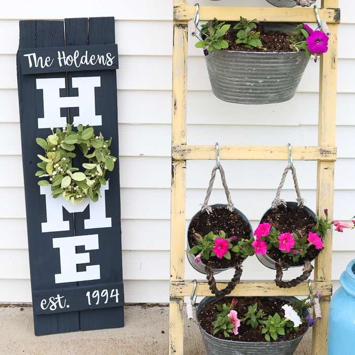 My homemade Home Sign with a Wreath next to a wooden hanging planter stand on my front porch