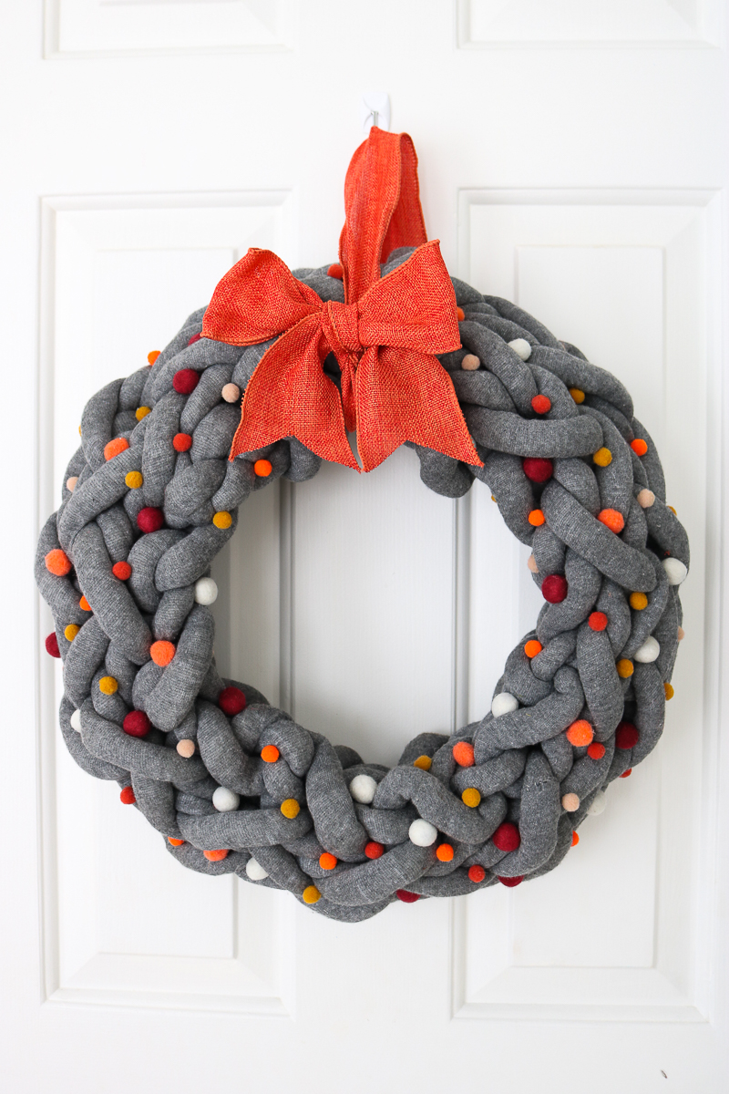 yarn wreath for fall with orange bow on front door