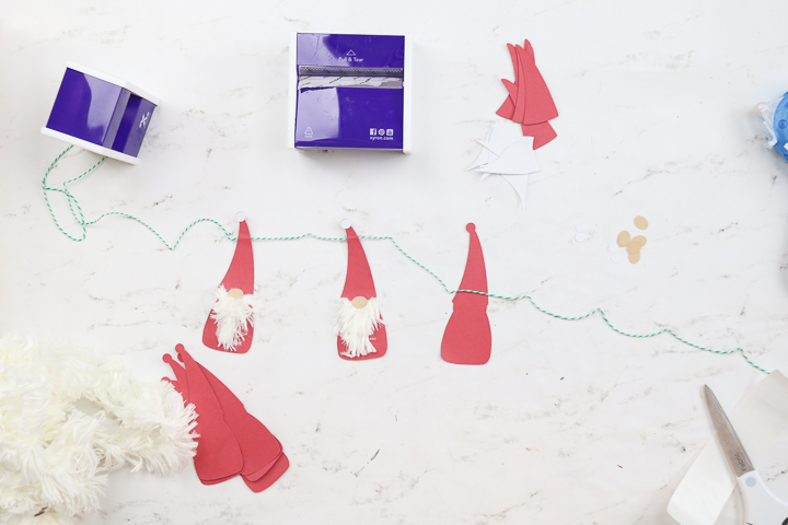 To assemble the Christmas gnome banner, attach the gnome body to the twine with hot glue