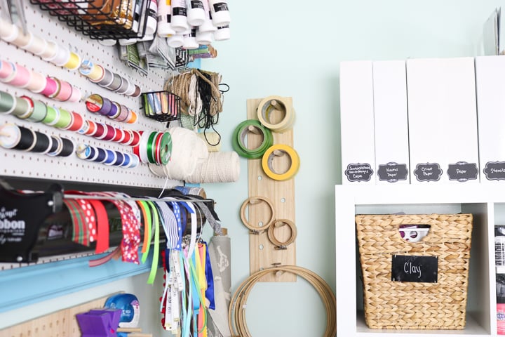 thread and ribbon organized on pegboard with embroidery hoops and basket