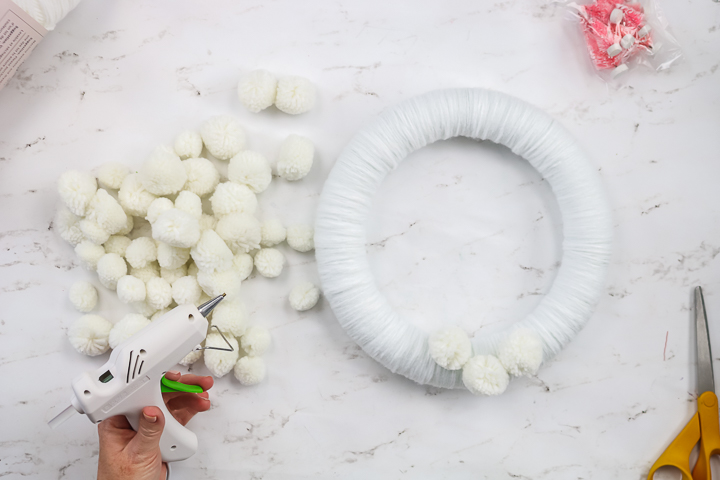 using hot glue to secure white pom poms to a wreath